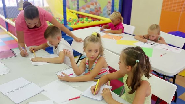 
 

smiling kids drawing together with tutor at hobby group indoors