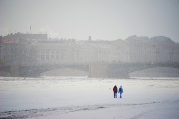 Two young people crossing on the ice of the river Neva in winter during snowfall in Central St. Petersburg.