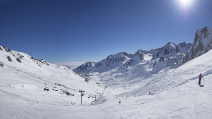 Unidentified skiers are on the snowy slope into  Grand Tourmalet ski resort against the mountain range in the French Pyrenees