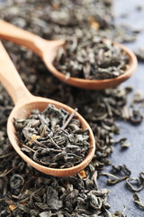 Heap of dry tea with wooden spoon on grey table