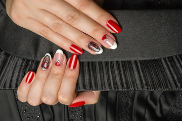 French manicure - beautiful manicured female hands with red black and white manicure with rhinestones  on black background