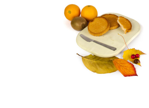 Two and a half bisquits on a wooden plate with two oranges, a kiwi and some autumn decoration.
