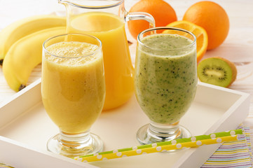 Healthy orange and kiwi smoothies with banana on white wooden background.