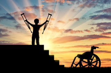 Happy disabled boy standing on sters with crutches in his hands and wheelchair © Prazis Images