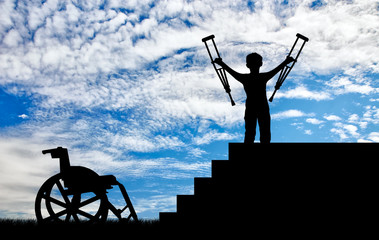 Happy disabled boy standing on sters with crutches in his hands and wheelchair © Prazis Images