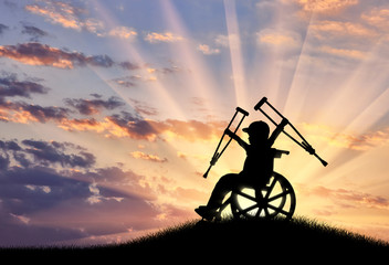 Obraz na płótnie Canvas Happy boy sitting in wheelchair with crutches sunset