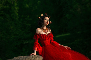 Young Countess in a luxurious red dress sitting of nature.