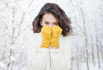 Beautiful natural young smiling brunette woman wearing knitted sweater and glove in the woods. Snowing snow winter concept.