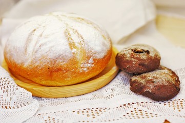 Dessert bread, dusted with powdered sugar, on a wooden Board and rye cakes after baking in the oven on a white lace tablecloth.