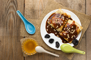 Pancakes with berries, fruits, chocolate, pine nuts and honey on white plate on a natural wooden board
