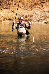 Happy fisherman pulls caught grayling from river