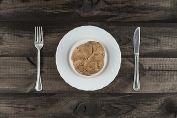 kaiser roll on white plate with fork and butter knife on wooden table
