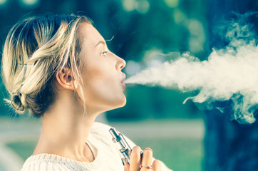 Teenage girl smoking with an electronic cigarette - obrazy, fototapety, plakaty