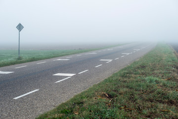 Rural road with traffic sign in dense mist. Geesteren. Achterhoek. Gelderland. The Netherlands.