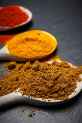 spices in wooden spoons over black stone background, top view