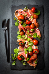 Salad with ham jamon serrano, cherry tomatoes, arugula, slate board