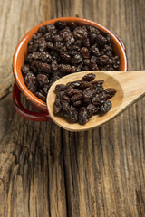 Raisins in a wooden spoon above Bowl On wood background