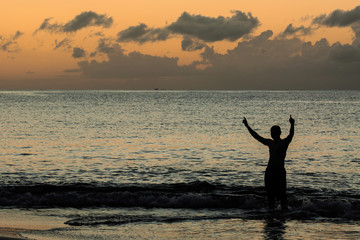 Man playing and put his hands into the sky  at sea in sunset, si