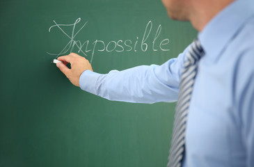 Businessman putting a cross over word impossible on blackboard