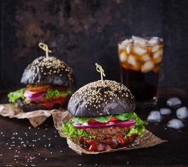 Beef burger with a black bun,with lettuce and mayonnaise and ketchup served on pieces of brown...