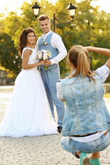 Young woman taking photo of happy wedding couple in park