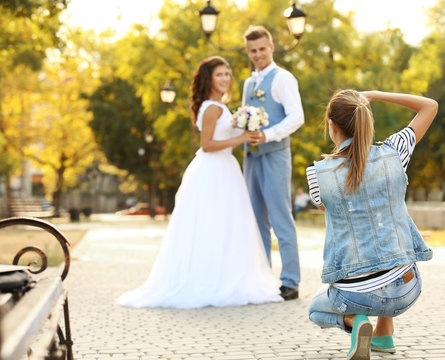 Young woman taking photo of happy wedding couple in park