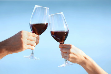 Two hands holding glasses with red wine on sea background