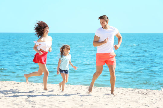 Family concept. Happy parents and daughter playing on the beach