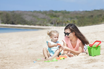 little baby girl playing sand toys with her mother at the beach