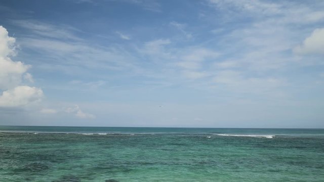 Airplane landing on island Bali airport under blue sea with waves on the horizon. Cinematic shot of overhead flying aircraft with shadow on beautiful ocean on cloudy sky background. Focal length 50 mm