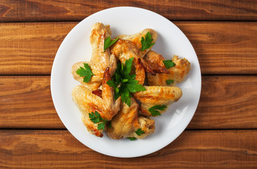 Plate with baked chicken wings and parsley on a wooden background