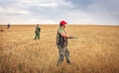 Group of hunters with a guns moving through the field