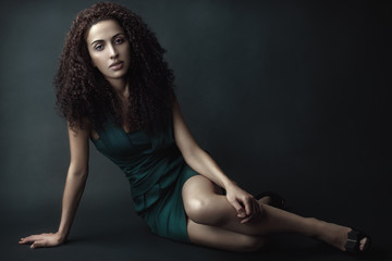 Fototapeta premium Fashion portrait of a beauty brunette girl with curly hair in green dress.