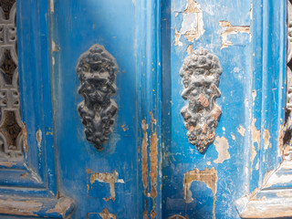 Old peeling door with various knobs and doorknockers and iron grid