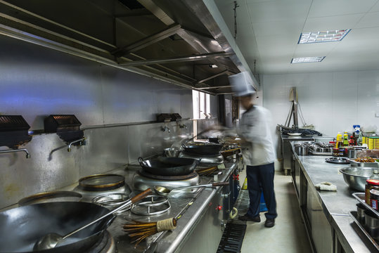 Chef in restaurant kitchen at stove with pan, doing flambe on food