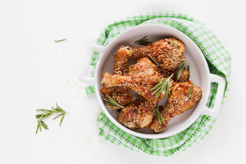 Chicken legs baked with sesame seeds in white dish, fresh rosemary. Top view.