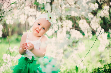 spring portrait of cute baby girl in green skirt enjoying outdoor walk in blooming garden