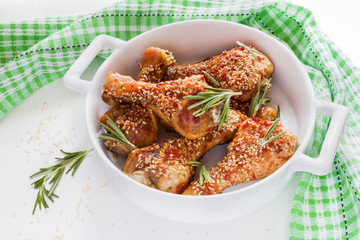 Chicken legs baked with sesame seeds in white dish, fresh rosemary.