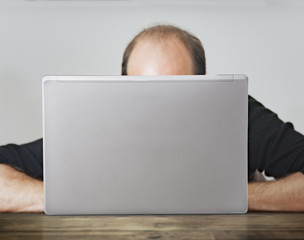 Bald man working behind a laptop on a wooden table