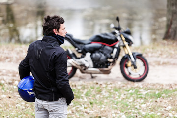 Biker standing near motorcycle holding his blue helmet.