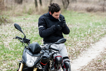 Fototapeta na wymiar Biker sitting on motorcycle and smoking his cigarettes