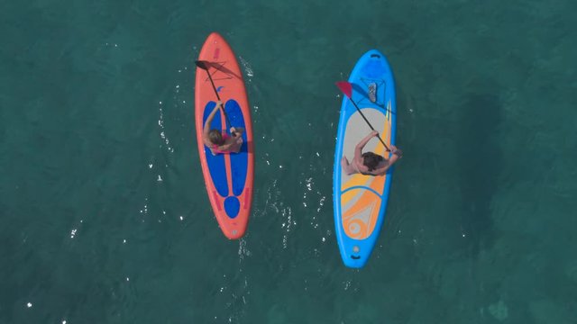 AERIAL, CLOSE UP: Girls stand up paddle surfing in parallel, paddling in rhythm