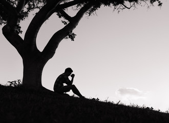Man praying. Religion concept. Young man with his hands folded together sitting under a tree. 