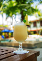 Yellow Pina Colada cocktail on a table on tropical island. Palm