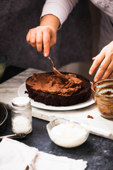 Hands spreading milk chocolate frosting onto a cake. Woman spreading chocolate on cake.