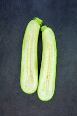 Two halves of fresh green zucchini isolated on dark gray slate s