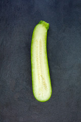 Two halves of fresh green zucchini isolated on dark gray slate s