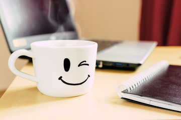 Smiling cup, notepad and laptop on the desk