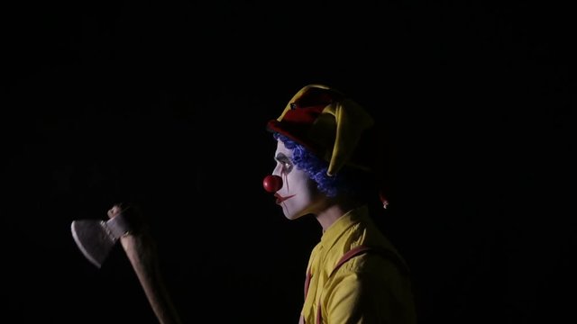 Scary clown with an axe in a dark room. Frightening jester, clown, buffoon. HD.