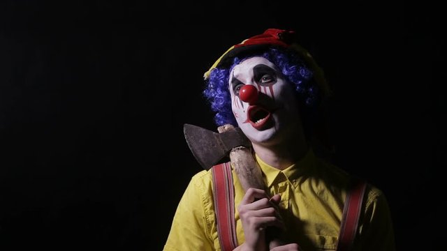 Scary clown with an axe in a dark room. Frightening jester, clown, buffoon. HD.